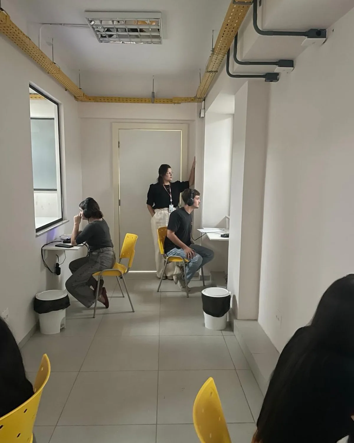 Alunos em atendimento prático com fones de audiometria em uma clínica-escola, acompanhados pela professora.