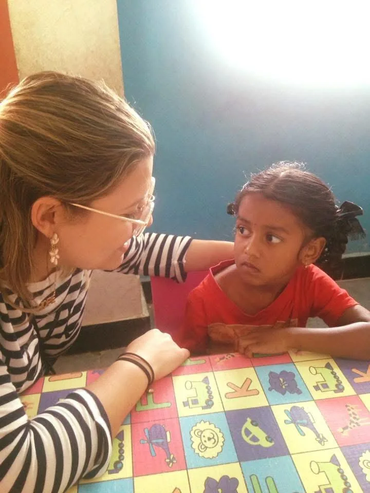 Dra. Tatiana conversa com uma menina apoiada em mesa colorida dentro de uma sala de atendimento infantil.