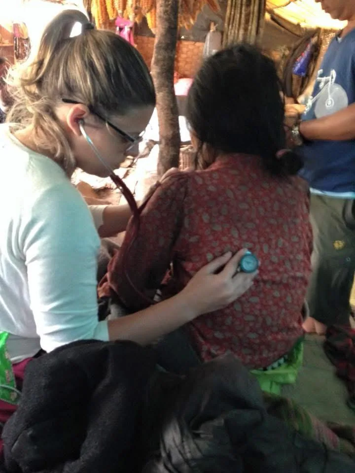 Dra. Tatiana ausculta as costas de uma mulher dentro de uma casa simples de comunidade rural.