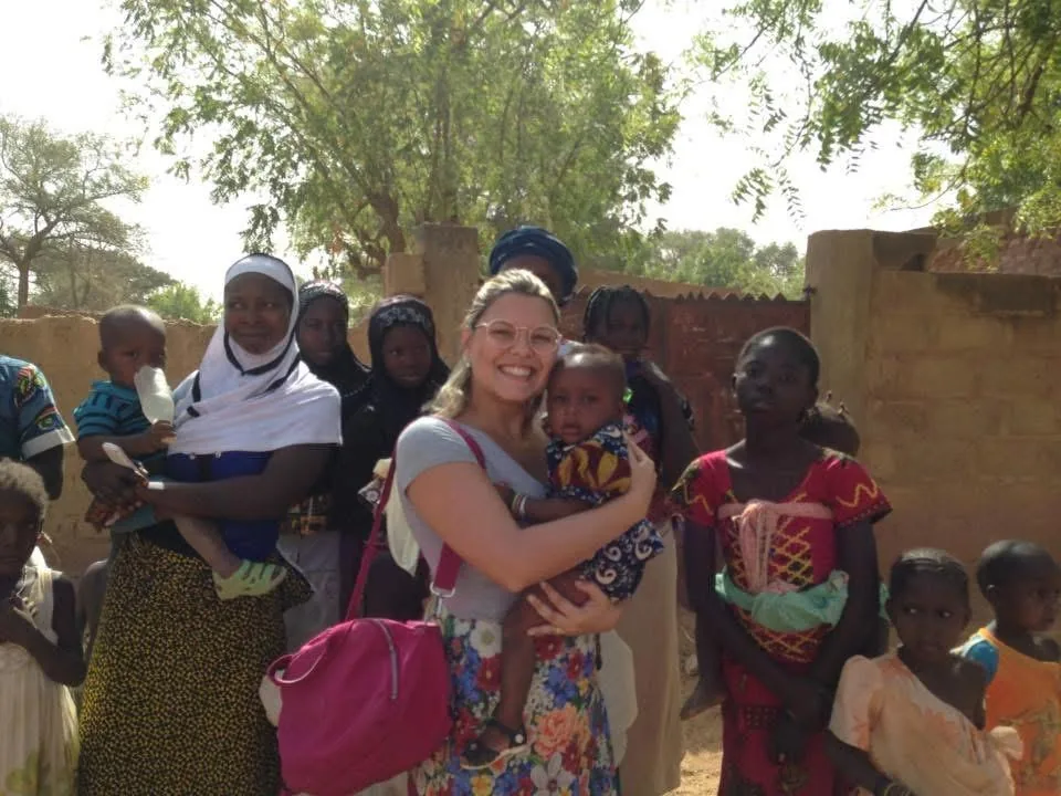 Dra. Tatiana segura um bebê no colo cercada por mulheres e crianças de uma comunidade africana.